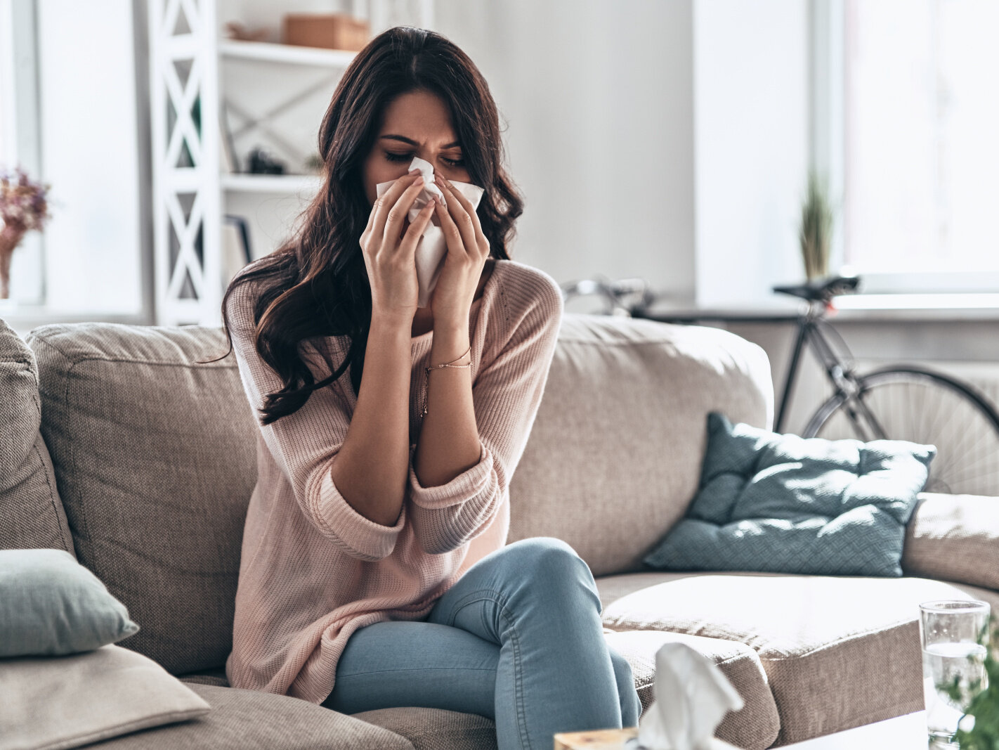 Cold and flu. Sick young woman blowing the nose using tissue paper while sitting on the sofa at home, Woman at home with flu or allergy symptoms cleaning her nose
