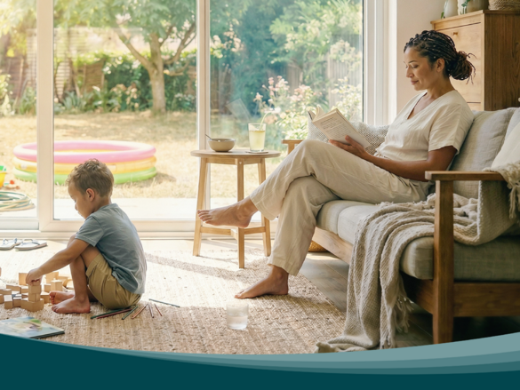 Living room with large windows facing the garden. Children play on a rug while a person reads on the sofa. Zehnder residential ventilation ensures air exchange.