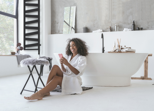 Smiling woman sitting in the bathroom on the floor with a smartphone in her hands