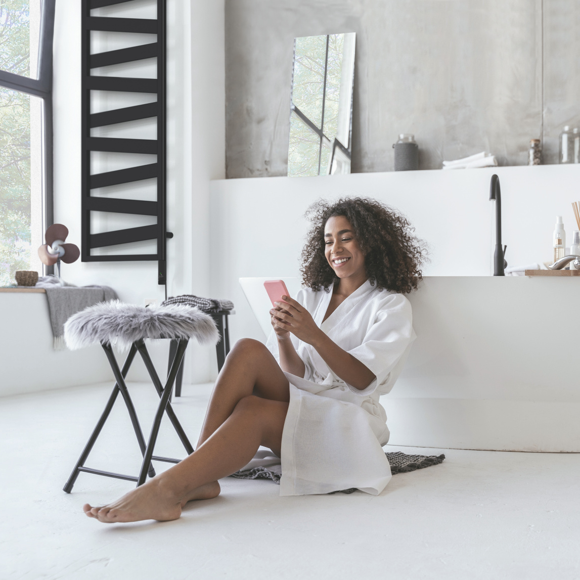 Smiling woman sitting in the bathroom on the floor with a smartphone in her hands